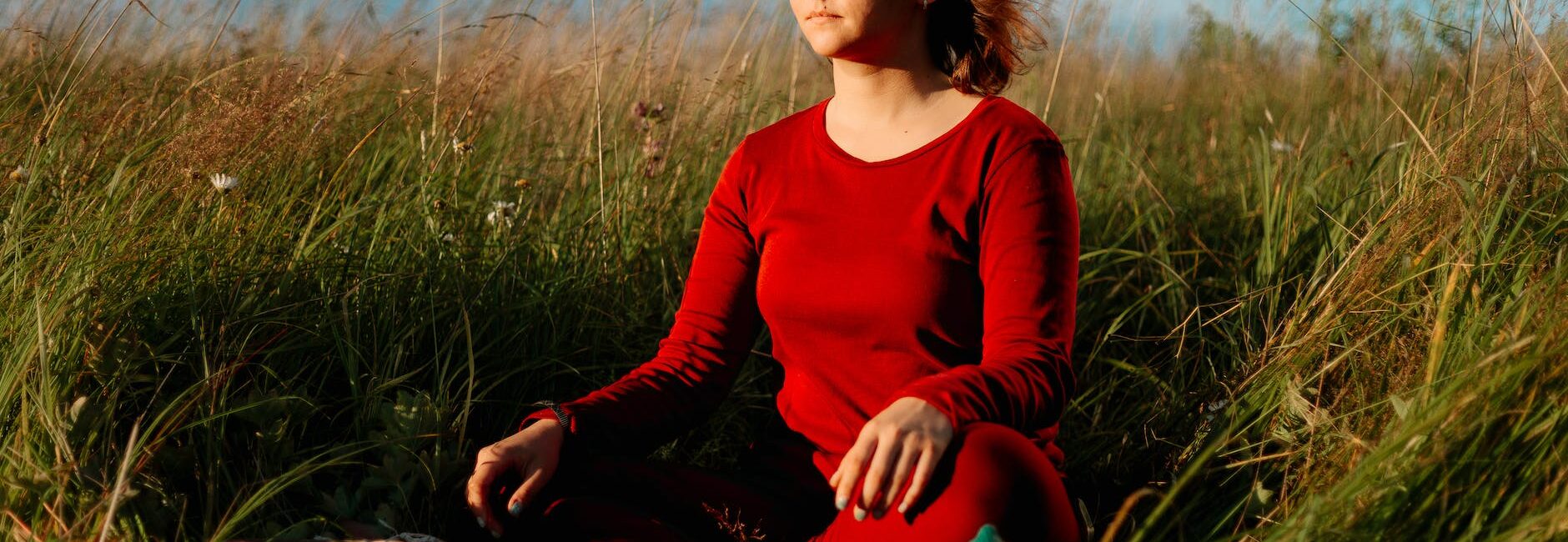 a woman in red long sleeve dress meditating on grass field