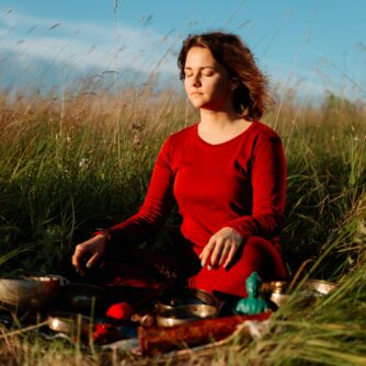 a woman in red long sleeve dress meditating on grass field