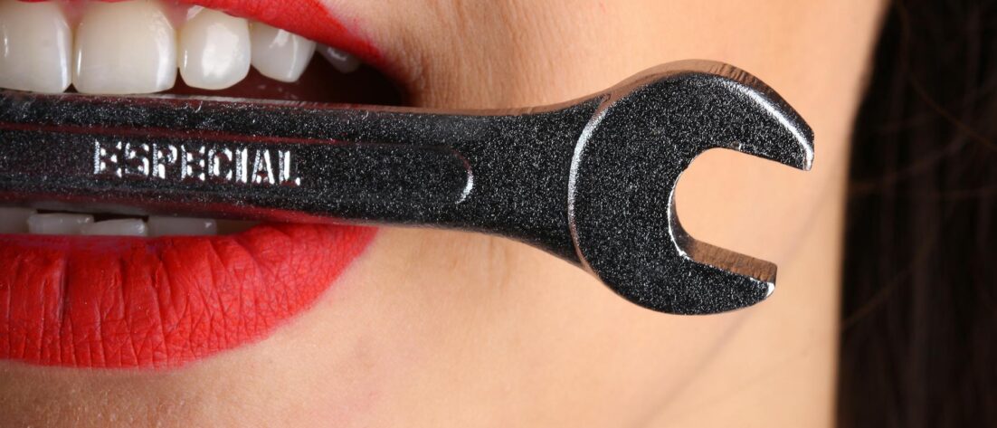 close view of woman with red lips biting gray special wrench