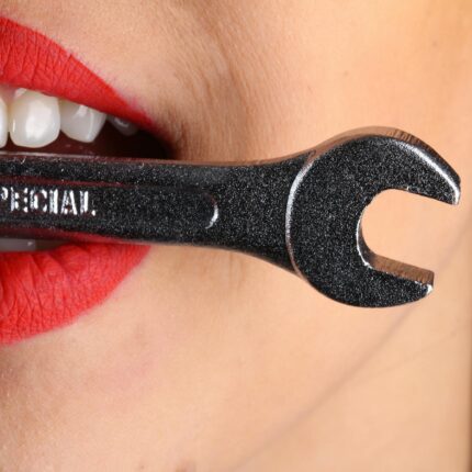 close view of woman with red lips biting gray special wrench