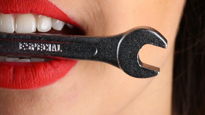 close view of woman with red lips biting gray special wrench