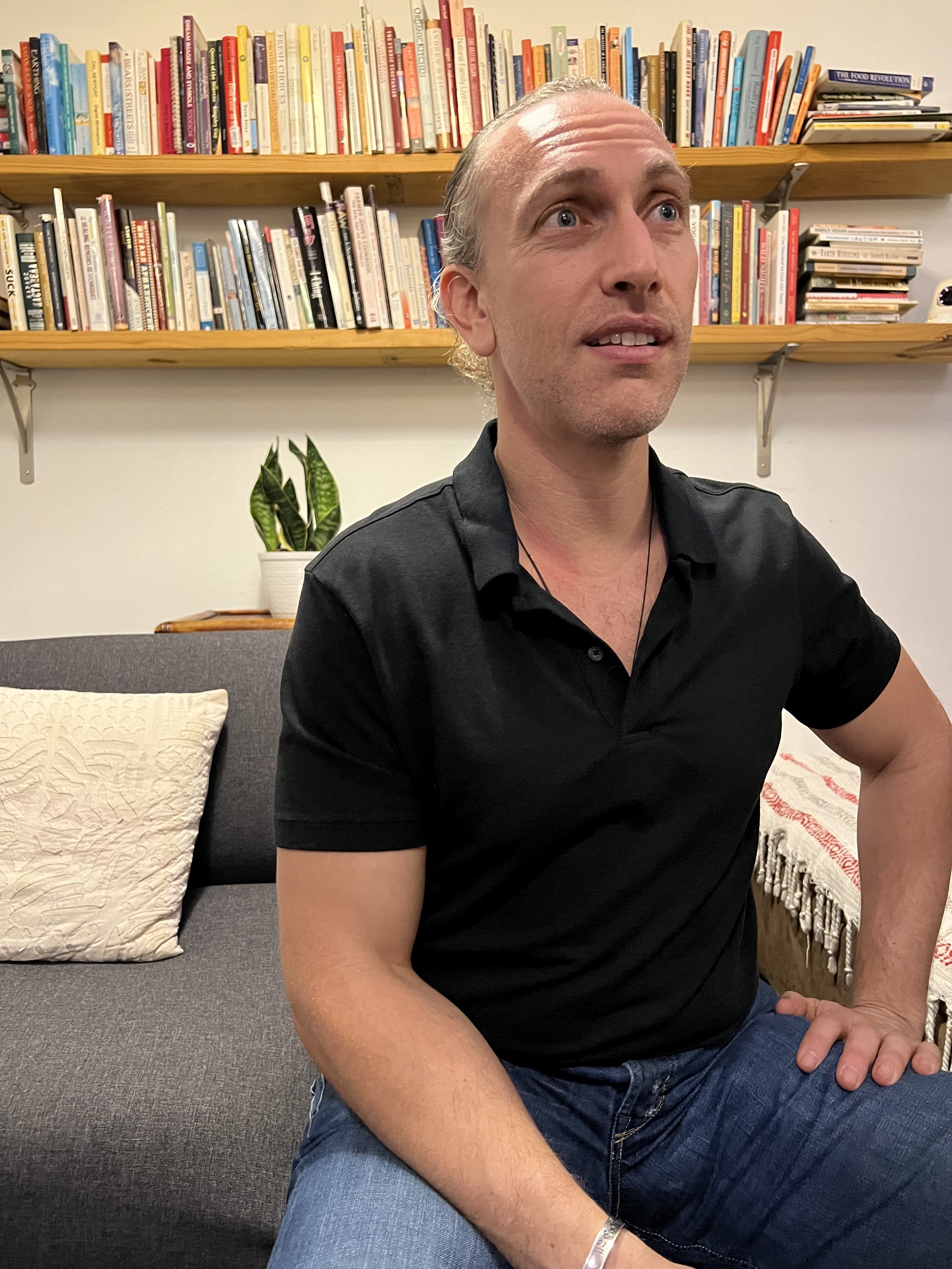 A seated speaker in conversation at the Zen Mystery oral-health talk, with bookshelves behind him